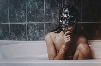 Woman wearing skull mask sitting in bathroom