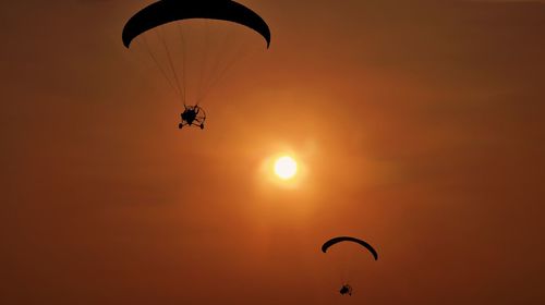 Low angle view of person paragliding against sky during sunset