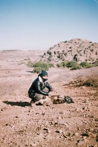 Man on rock in desert against clear sky