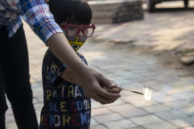 Midsection of mother and son holding sparkler while standing outdoors