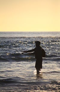 Silhouette man fishing in sea at sunset