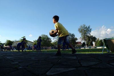 Boy playing soccer on field against sky