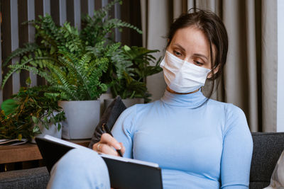 Woman in protective mask on the couch with notepad in hand