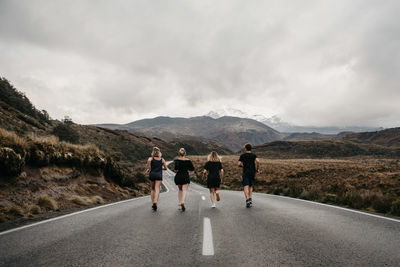 Friends running on road against sky