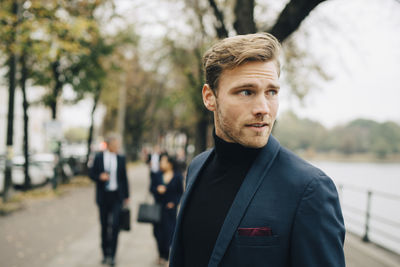 Contemplating businessman looking away while standing in city