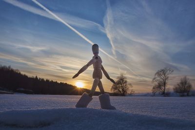 Woman standing on snow covered tree during sunset