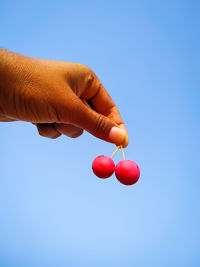 Low angle view of hand holding red against blue sky