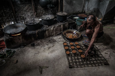 Shirtless man serving food in bowls by wood burning stove in kitchen