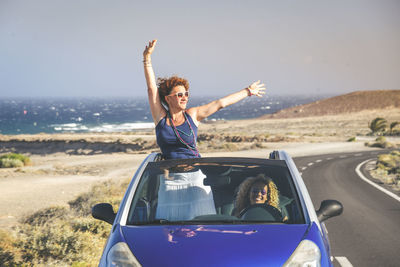 Happy friends enjoying in car on road with sea in background
