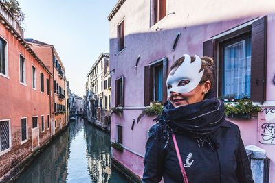 Woman standing by canal amidst buildings