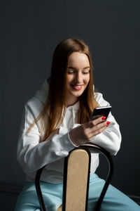 Young woman using phone while sitting against black background