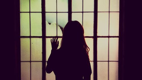 Silhouette of woman looking through window