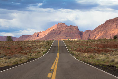 Empty road leading towards rocky mountains against sky