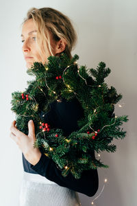 A young elegant woman holds a decorated christmas wreath on her shoulder. creative portrait