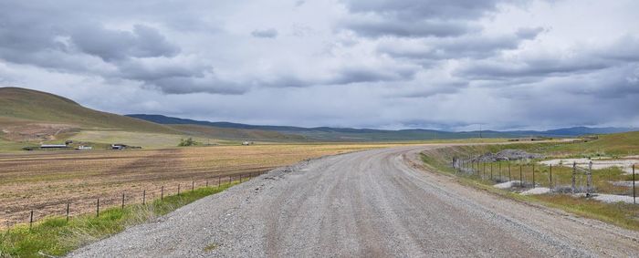 Dirt road amidst field against sky