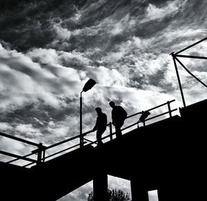 Silhouette men standing on bridge against sky