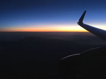 Airplane wing over silhouette landscape against clear sky