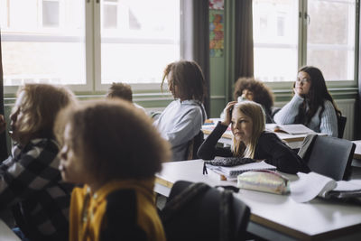 Bored girl leaning on elbow while sitting at desk during lecture in classroom