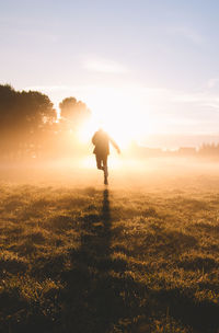 Rear view of silhouette man running on field against sky during sunset
