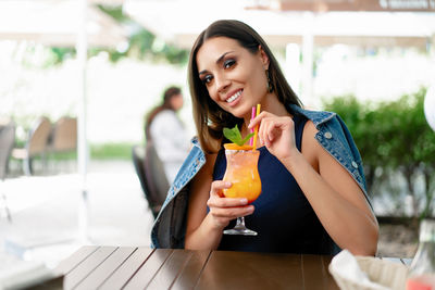 Young woman with drink sitting at sidewalk cafe