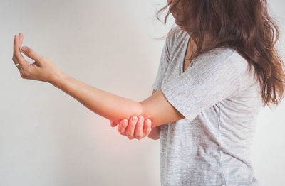 Woman holding aching elbow while standing against white background