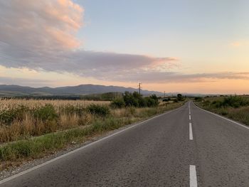 Road by landscape against sky during sunset