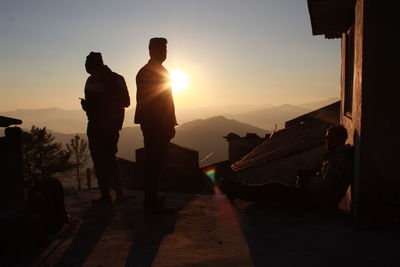 Silhouette men standing on building terrace against sky during sunset