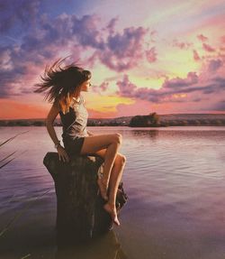 Woman sitting by lake against sky during sunset