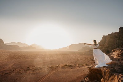 Woman sitting on desert against clear sky
