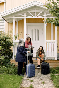 Multi-generation family waiting with luggage outside house