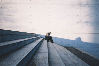 Side view of woman sitting on steps against gray wall