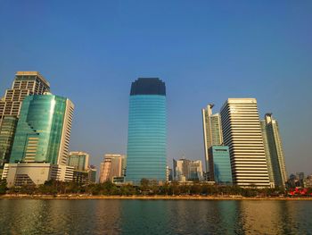 Modern buildings by river against clear blue sky