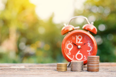 Close-up of red alarm clock with coins on wooden table