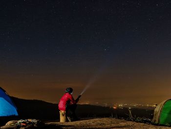 Rear view of man standing on field against sky at night