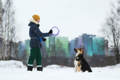 Man playing with dog in snow against sky