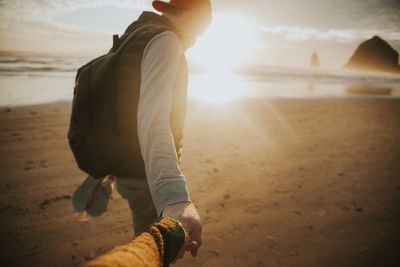 Cropped hand holding man at beach during sunset