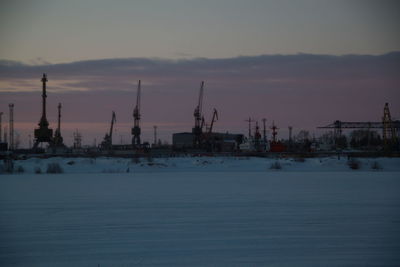 Cranes at harbor against sky during sunset