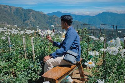 Side view of man sitting on field against mountain