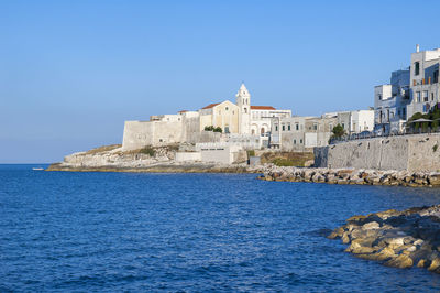 Buildings by sea against clear blue sky