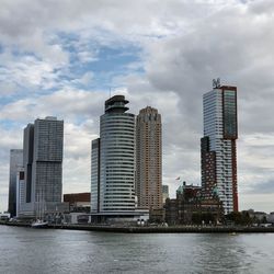 Modern buildings by river against sky in city