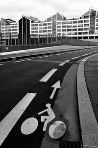 Arrow sign on road in city against sky