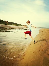 Full length of boy jumping while running at beach