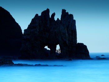 Rock formations in sea against clear blue sky