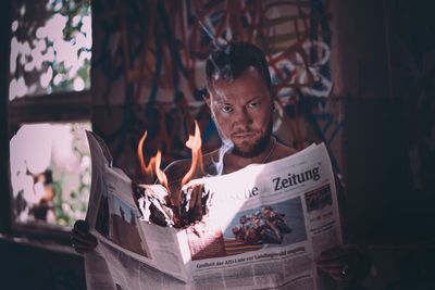 Portrait of young man holding burning newspaper