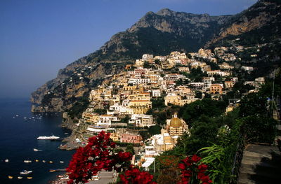 Buildings by mountains and sea against sky