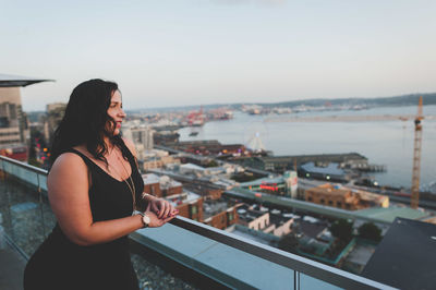 Beautiful woman leaning on railing against sky