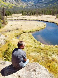 High angle view of mature man sitting on cliff against river