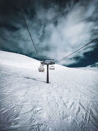 Ski lift over snow covered field against sky