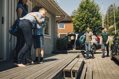 Mother embracing son while gay couple walking towards house during sunny day