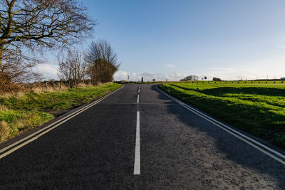 Empty road amidst field against sky